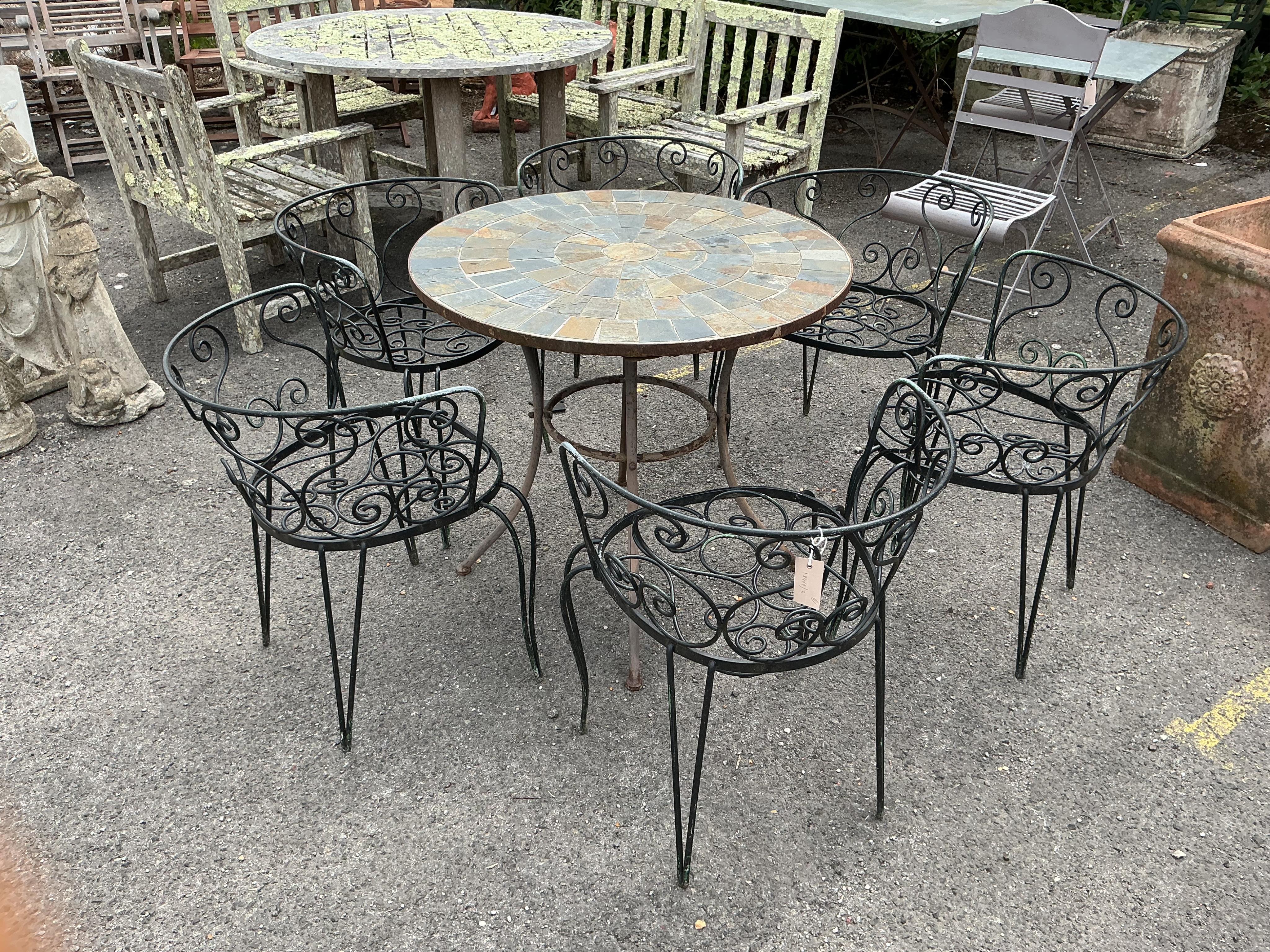 A circular stone mosaic topped garden table, diameter 80cm, height 72cm and six wrought iron garden chairs